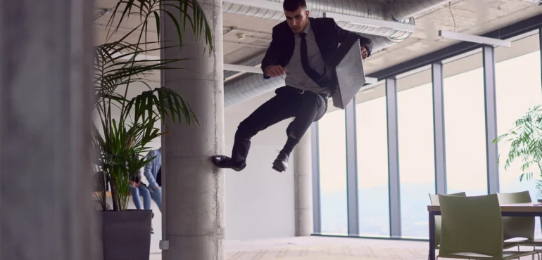 un agile uomo d'affari in ufficio cpn abiti e valigetta da lavoro che salta a un metro d'altezza appoggiandosi a una delle colonne in un ufficio marketing